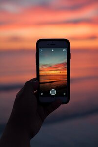 Person Holding Iphone Taking Picture on Ocean With Sunset Background photo