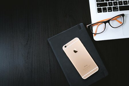 Gold Iphone 6 on Black Case Besides Eyeglasses on Silver Macbook