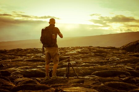 Man Beside Tripod on Rocks during Golden Hour photo