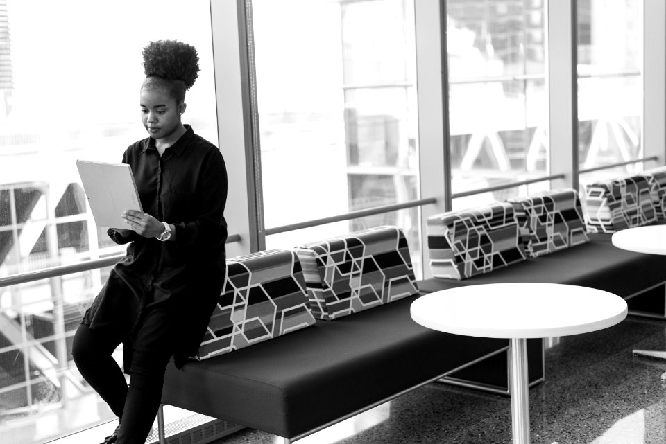 Grayscale Photo Of Woman Holding Gray Notebook On Sofa Near Glass Window