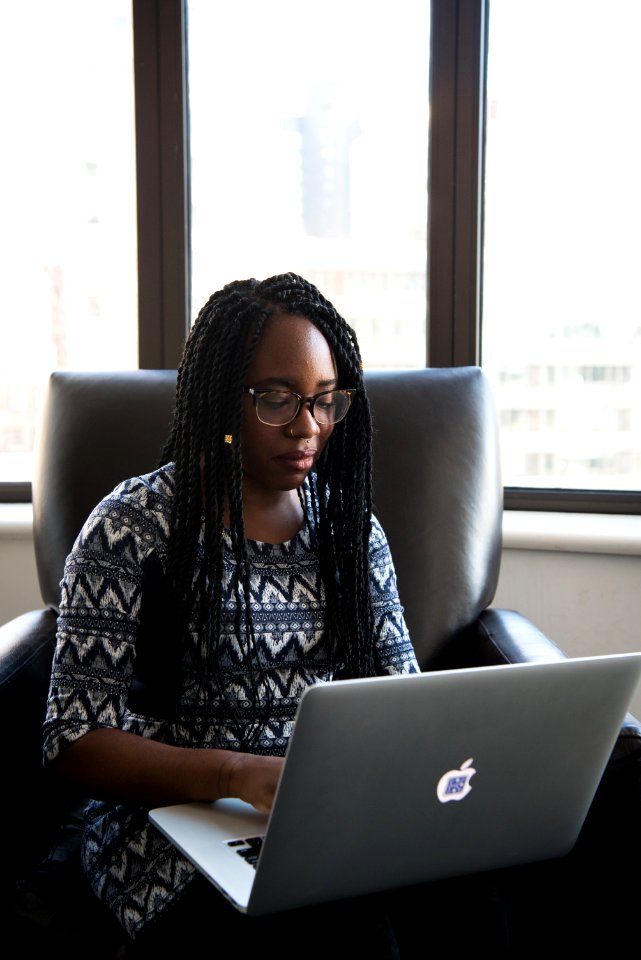 Woman In Black And White Blouse Sitting On Black Leather Chair Holding Her Laptop