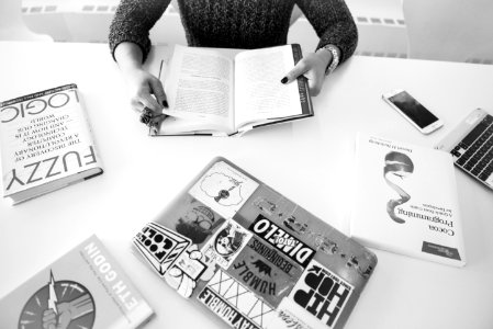 Grayscale Photo Of Person Sitting Near Table With Books photo