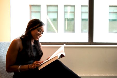 Woman Wearing Black Crew-neck Sleeveless Top Sitting Of Gray Sofa While Reading Book photo