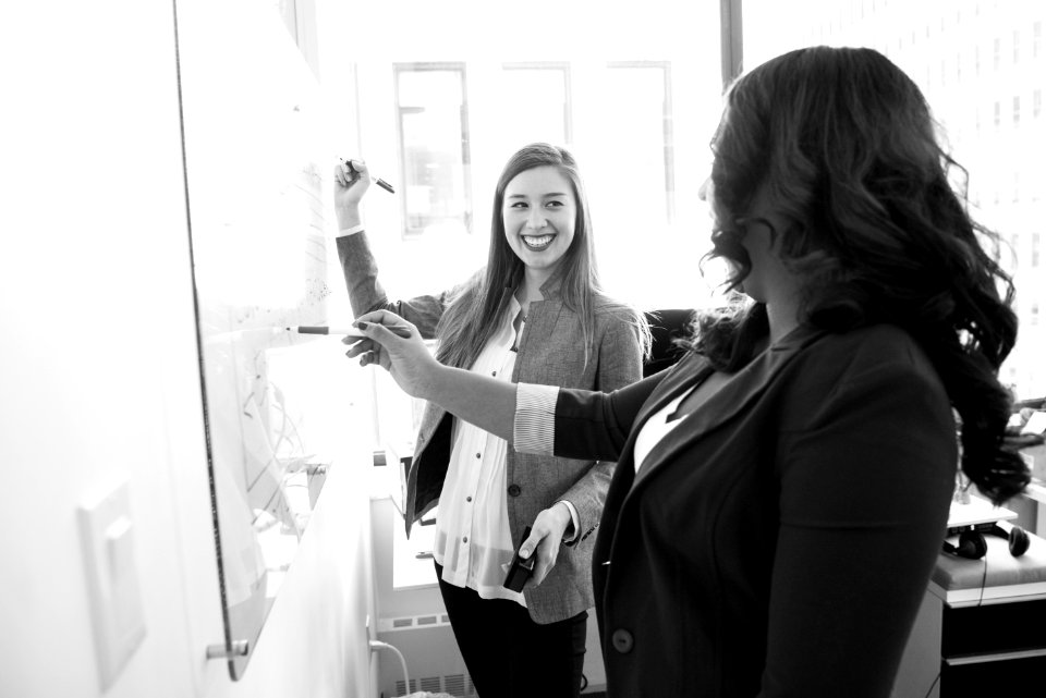 Two Smiling Woman Writing On Board