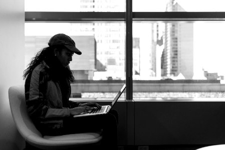Grayscale Photo Of Woman Wearing Cap And Jacket Using Laptop photo