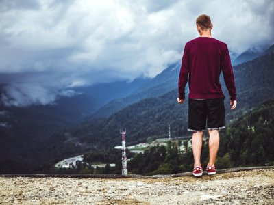 Man Wearing Maroon Sweater And Black Shorts Standing In Front Of Mountain photo
