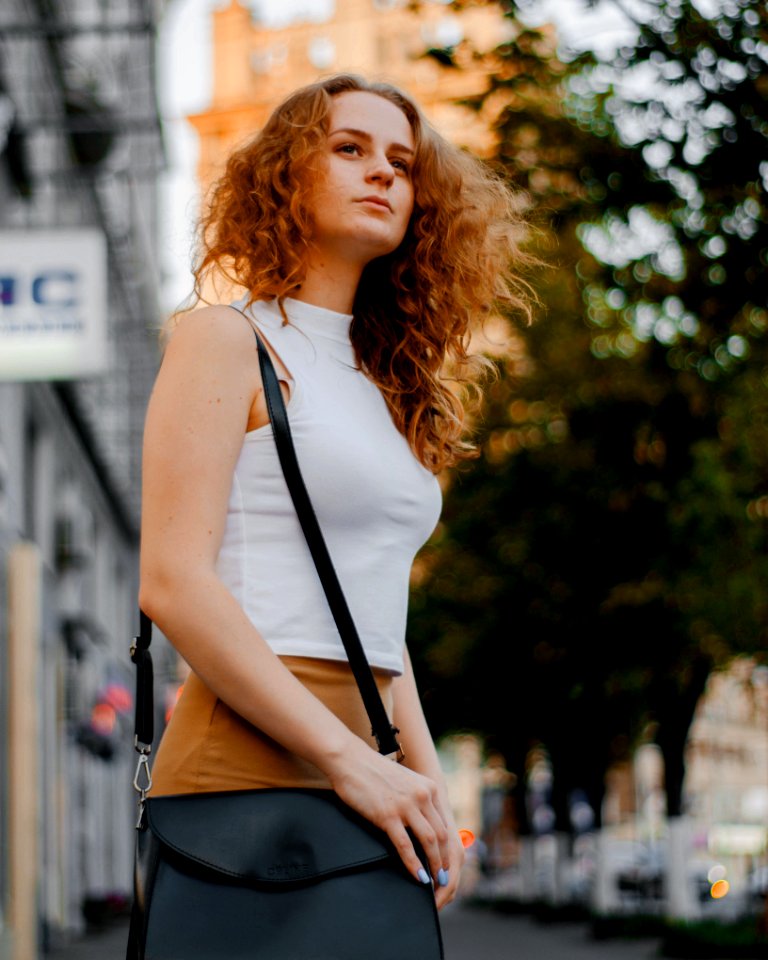 Woman In White Turtleneck Sleeveless Top And Brown Bottoms Holding Black Leather Crossbody Bag Outfit