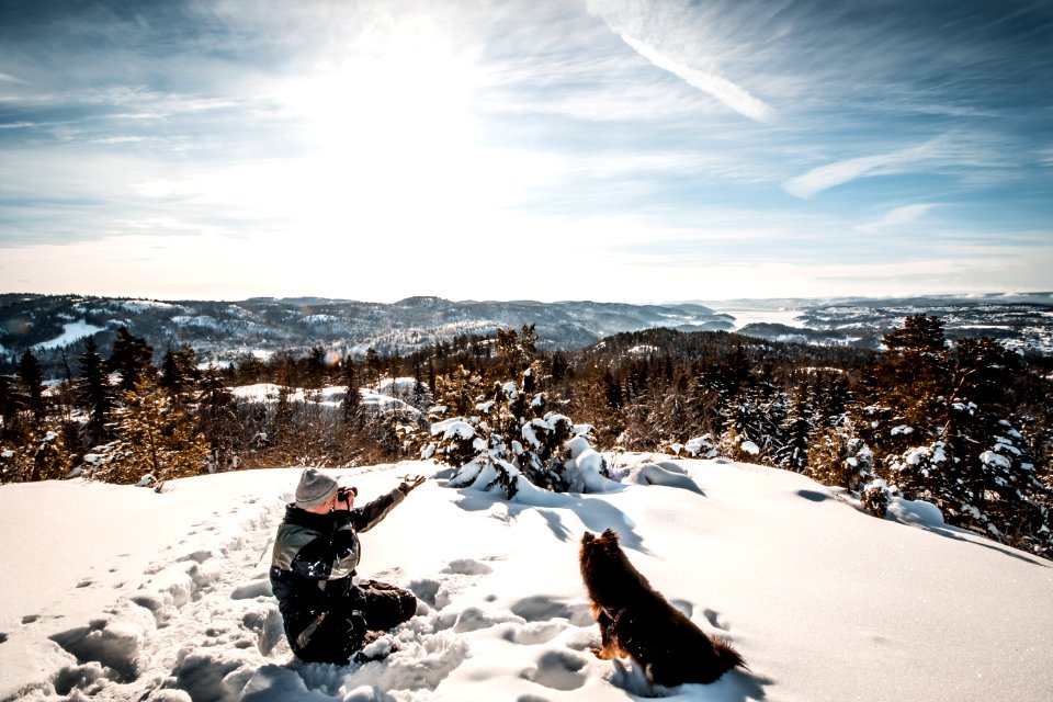 Man Sitting Near A Dog Holding A Camera While Taking Picture Of The Landscape