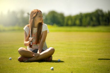 Woman In White Scoop-neck Shirt And Blue Shorts Holding A Golf Club Sitting On Golf Field photo