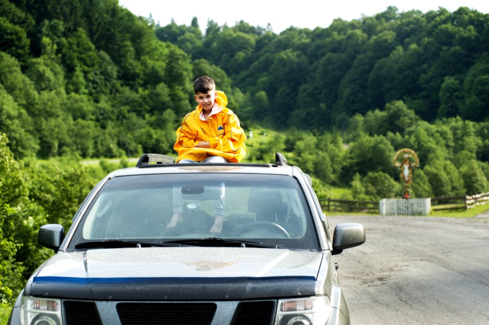 Child In Yellow Jacket Sitting On Roof Of Nissan Frontier Through The Sunroof