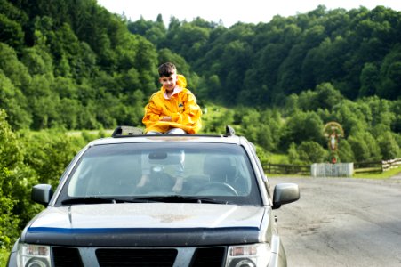 Child In Yellow Jacket Sitting On Roof Of Nissan Frontier Through The Sunroof