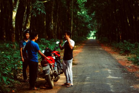 Three Men Standing Beside Red Motorcycle Surrounded With Green Trees photo