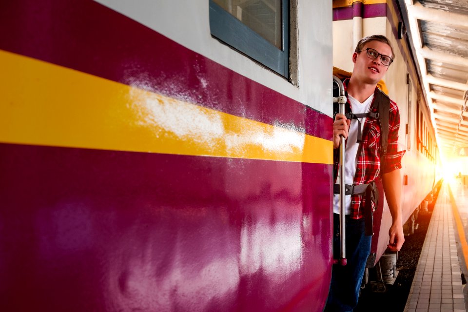 Man Wearing Red Button-up Shirt And Blue Jeans Holding Silver Train Side Rail