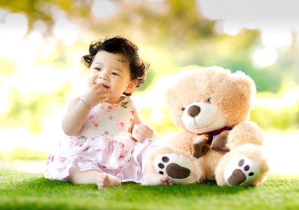 Baby Sitting On Green Grass Beside Bear Plush Toy At Daytime photo