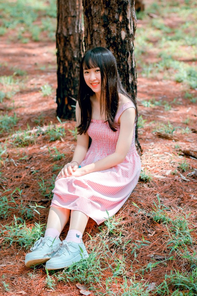 Girls Pink Sleeveless Dress Sits Beside Black Tree Trunk At Daytime