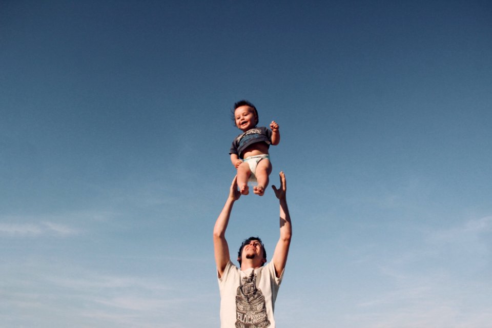 Photo Of Man In Raising Baby Under Blue Sky