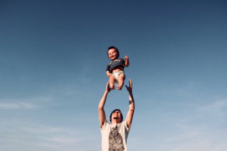 Photo Of Man In Raising Baby Under Blue Sky