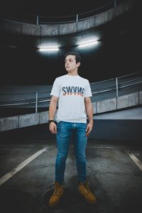 Man Wearing White T-shirt And Blue Jeans Standing On Black Concrete Floor photo