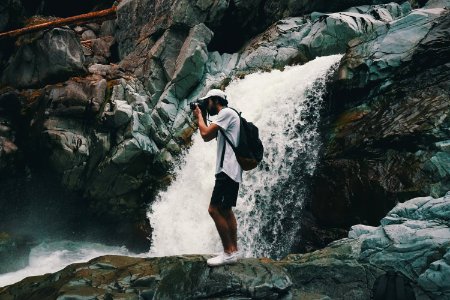 Man Wearing White T-shirt Holding Dslr Camera Near Waterfall