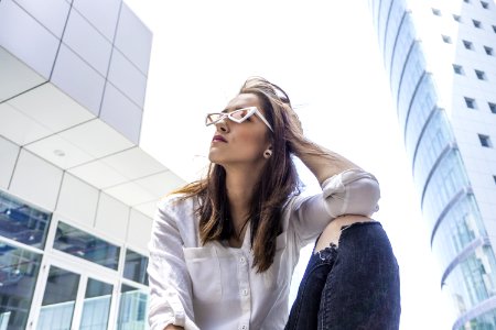 Low Angle Photography Of Woman In White Shirt Sitting Beside Buildings
