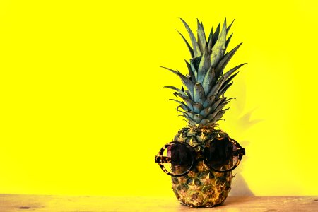 Green Pineapple Fruit With Brown Framed Sunglasses Beside Yellow Surface photo