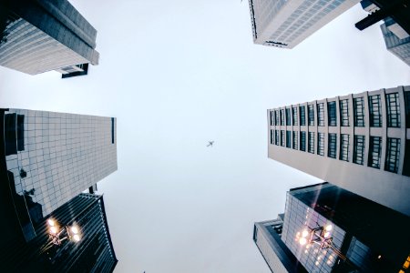 Low Angle Photography Of Airplane Flying Above High Rise Buildings photo