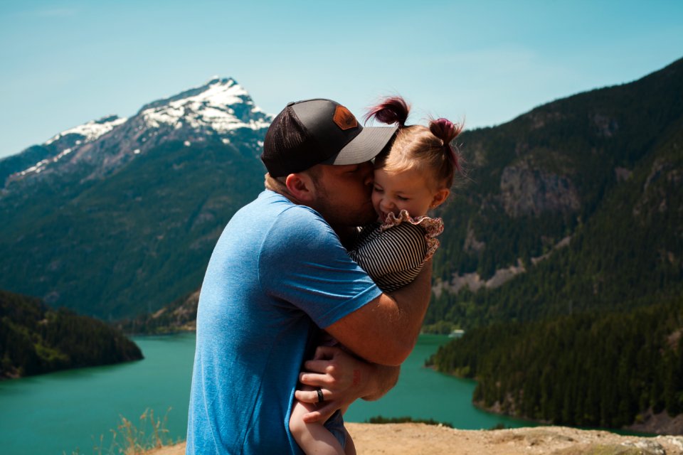 Man Wearing Blue Crew-neck T-shirt Holding Girl Near Mountains photo