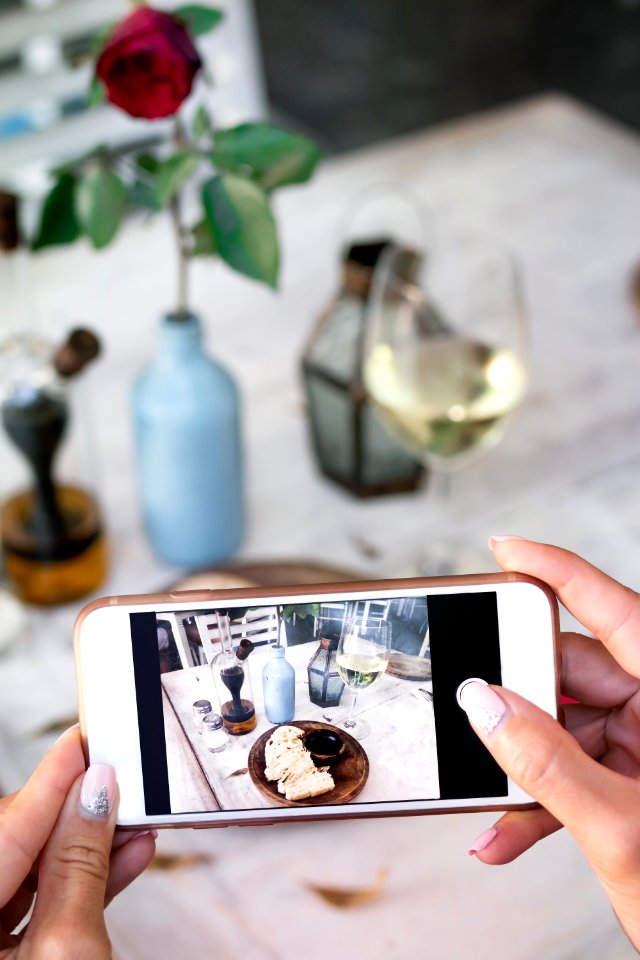 Woman Taking Photo Of Bread And Wine On Her Smartphone In Restaurant