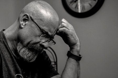 Grayscale Photo Of Man Thinking In Front Of Analog Wall Clock