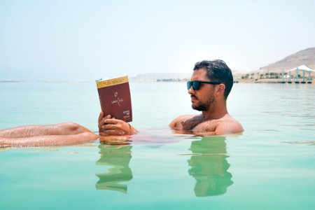Man Wearing Sunglasses Reading Book On Body Of Water photo