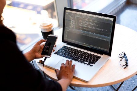 Person Looking At Phone And At Macbook Pro photo