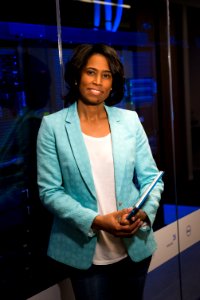 Woman In Teal Blazer Coat And Black Pants Holding A Tablet