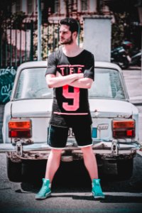 Man Wearing Black Scoop-neck T-shirt And Black Gym Shorts Standing Behind White Vehicle photo