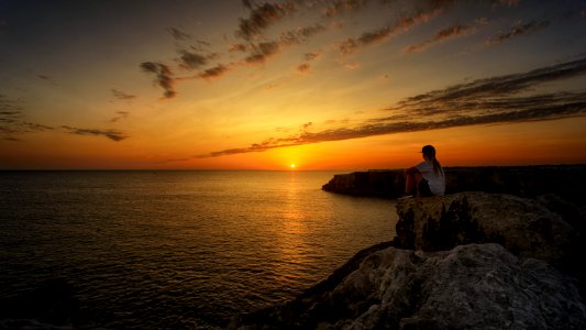 Photo Of Person Sitting On Rock During Sunset photo