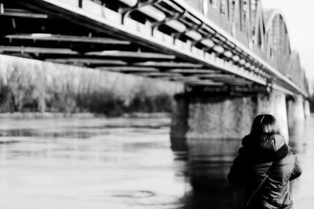 Grayscale Photo Of Person Wearing Jacket Near Bridge photo