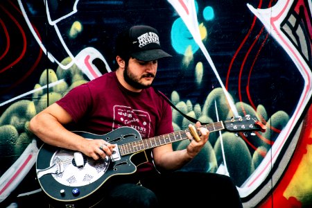 Man In Red Shirt Playing Resonator Guitar Near Wall With Black And Green Painting photo