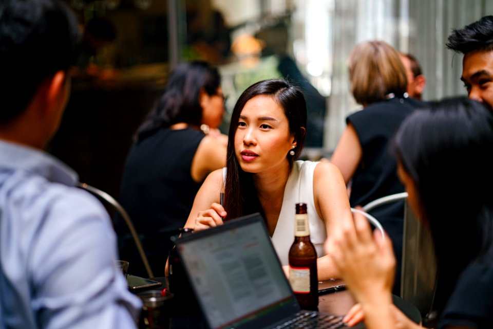Woman Wearing White Top Sitting Near Table With People