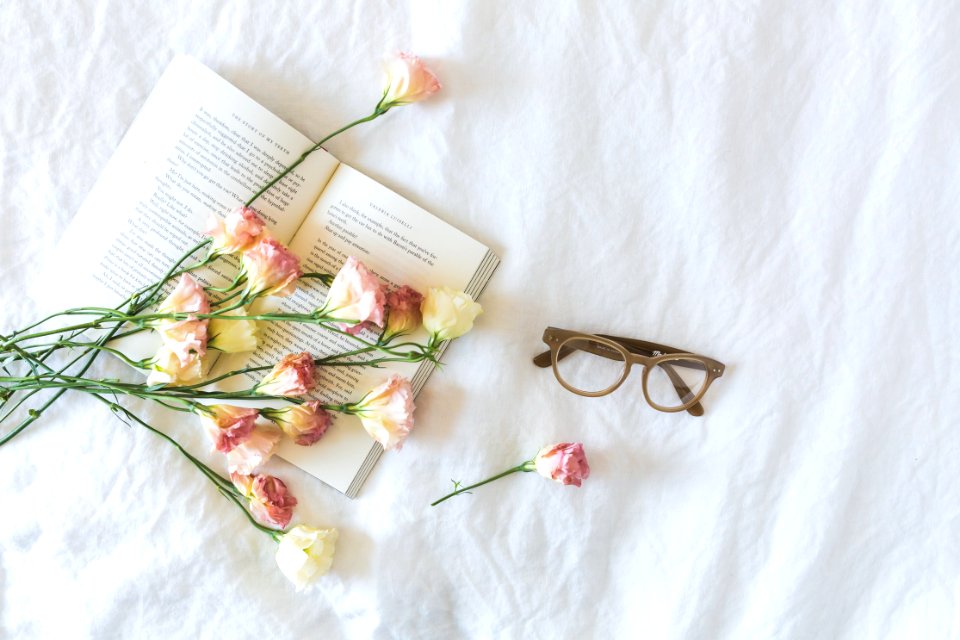 White And Pink Flowerson A Book Beside Eyeglasses
