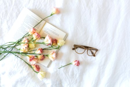 White And Pink Flowerson A Book Beside Eyeglasses