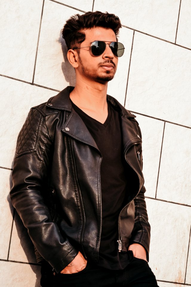 Man In Black Leather Jacket Leaning On White Concrete Wall