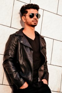 Man In Black Leather Jacket Leaning On White Concrete Wall photo