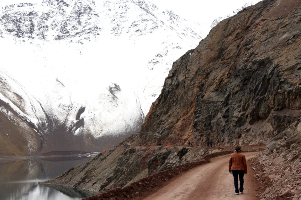 Woman With Brown Jacket Walking Beside Body Of Water