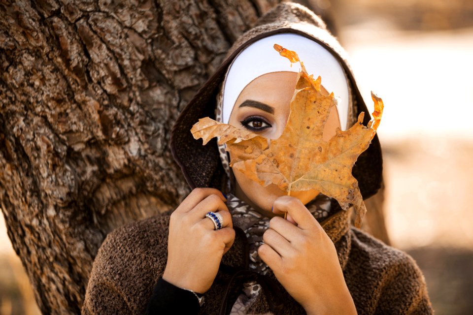 Woman Leaning On Brown Tree Holding Brown Leaf Covering Her Face