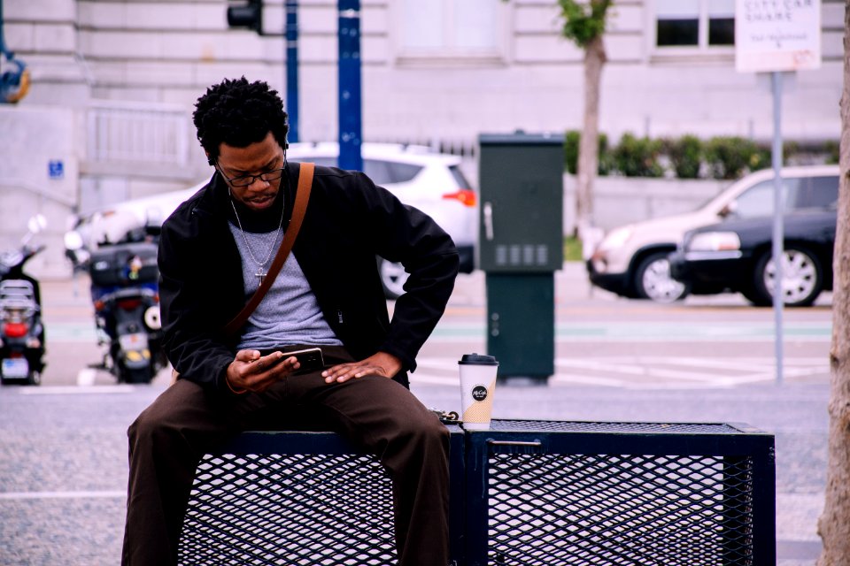Man Wearing Black Bomber Jacket And Holding Smartphone