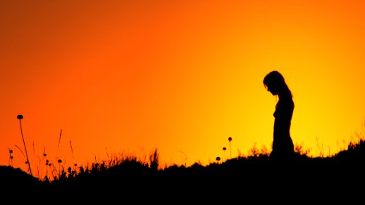 Silhouette Of Woman Standing On Grass Field During Sunset photo