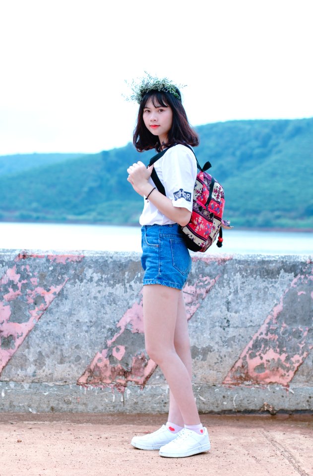 Photo Of Woman With Red And Black Backpack Standing Near Concrete Fence