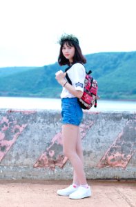 Photo Of Woman With Red And Black Backpack Standing Near Concrete Fence