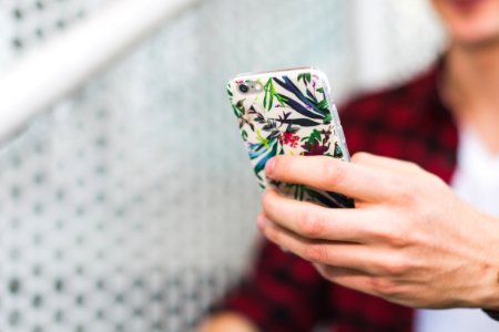 Person Holding Smartphone With White And Green Floral Case photo