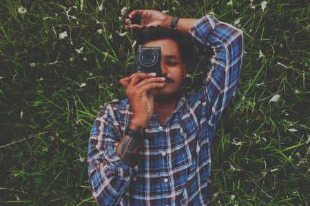 Man In Blue Dress Shirt Holding Camera White Laying On Grass photo