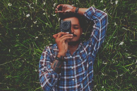 Man In Blue Dress Shirt Holding Camera White Laying On Grass